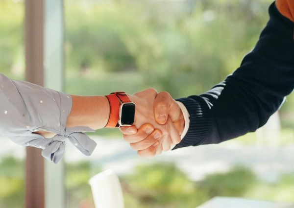 pexels-photo-6775120-6775120 Close-up of a handshake between two adults, one wearing a smartwatch, set in an outdoor environment.